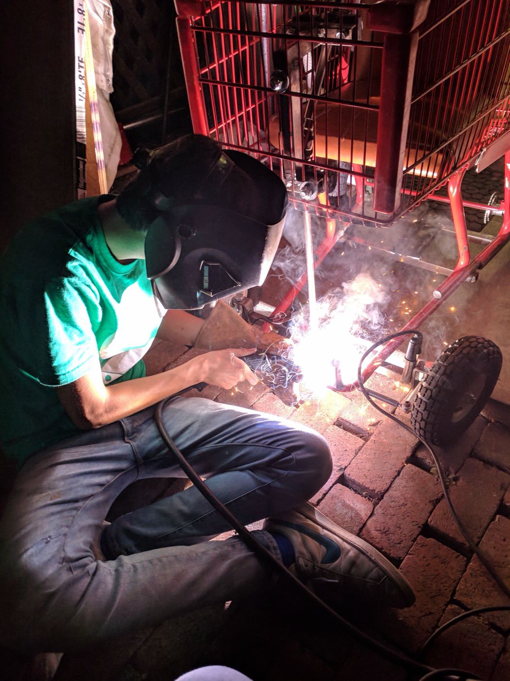 Spencer welding the shopping-cart go-kart frame at night, sparks flying