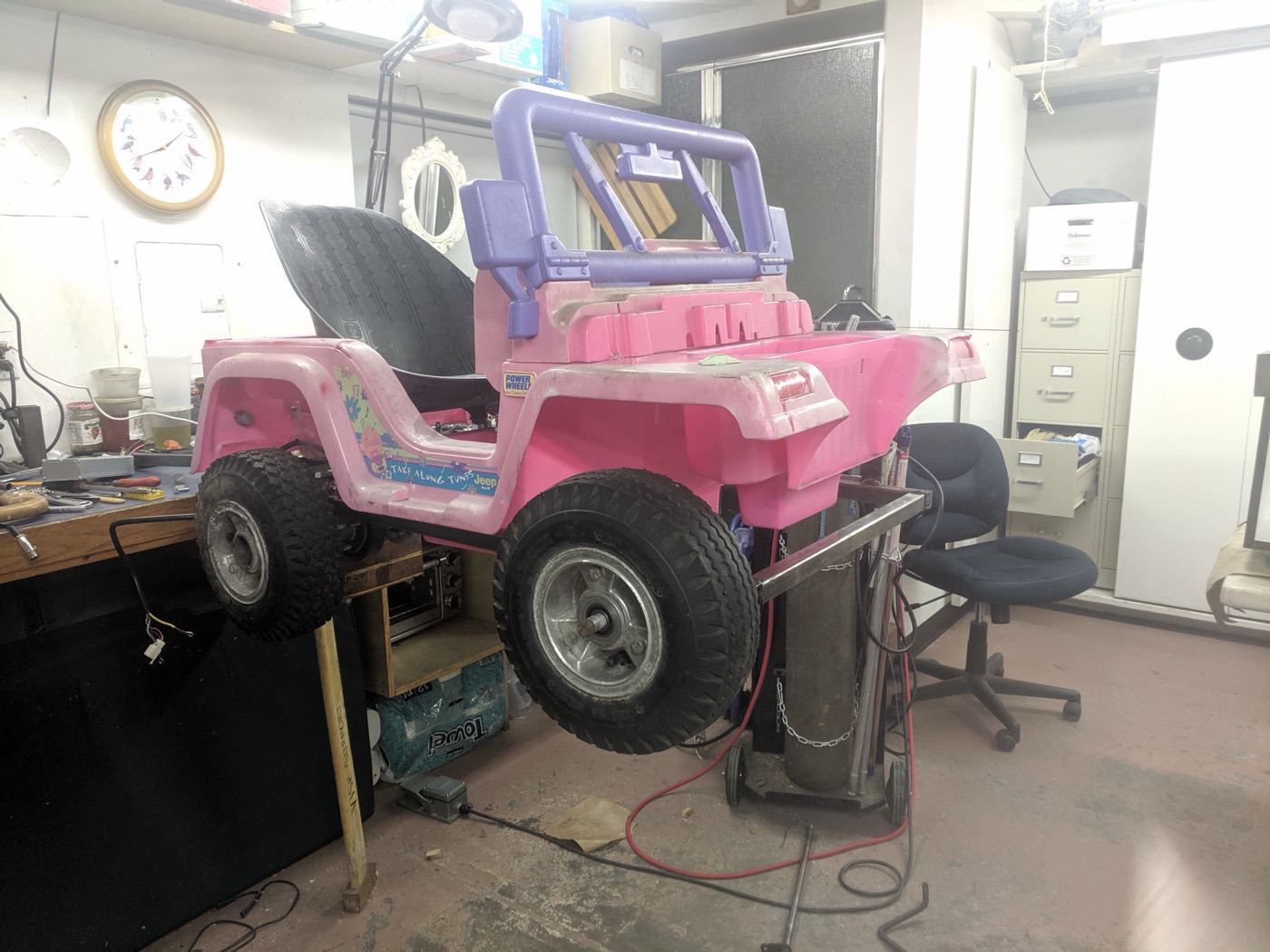 A pink Barbie Jeep up on a workbench mid-modification