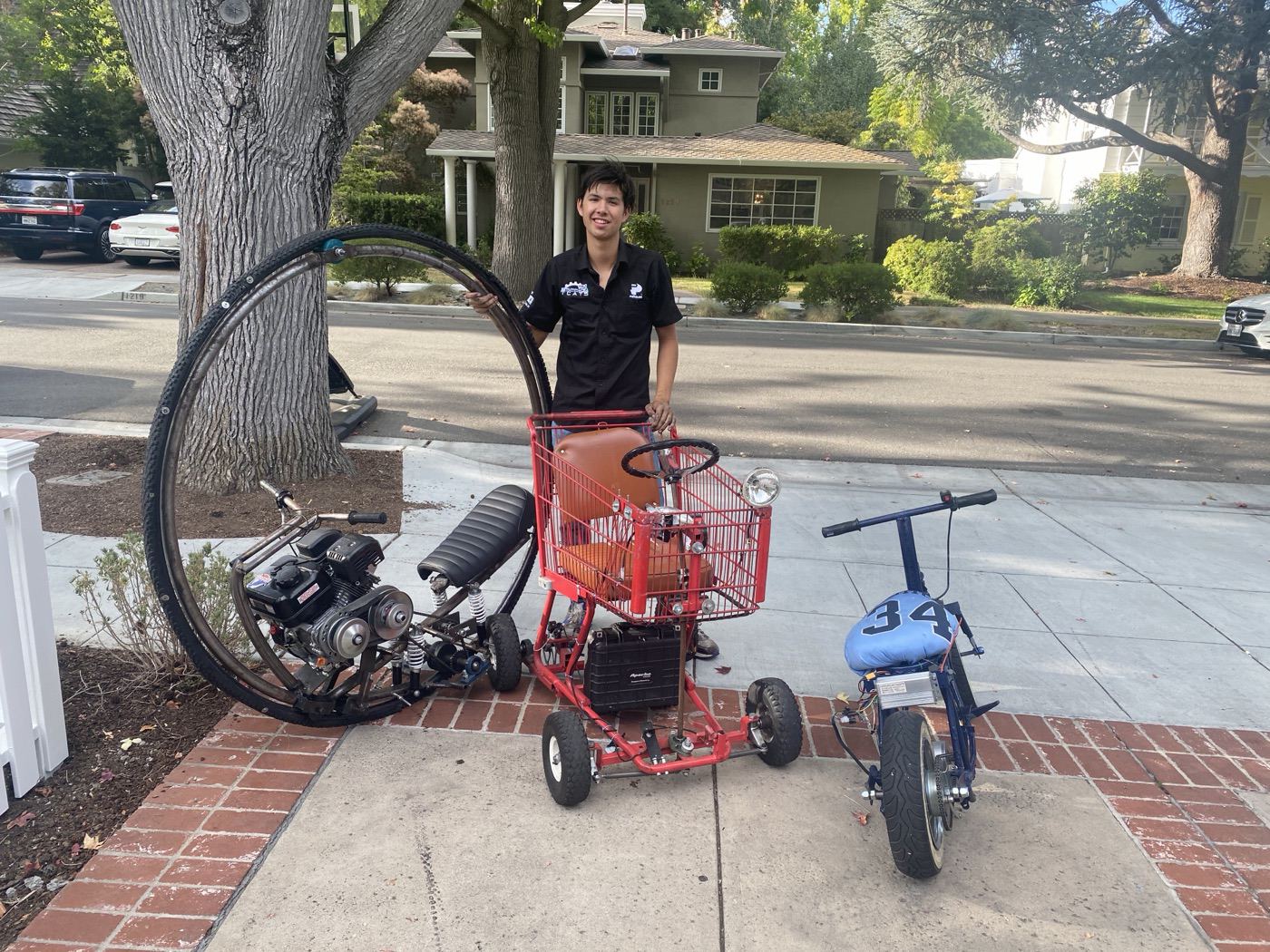 Spencer standing with the monowheel, shopping-cart go-kart, and electric mini-bike