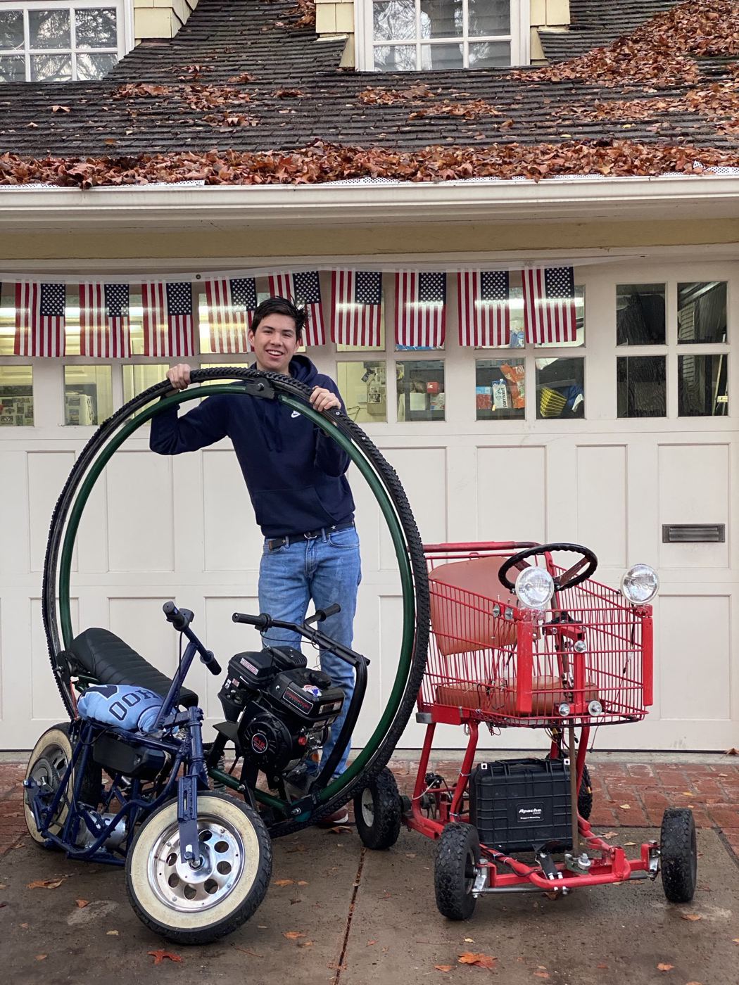 Spencer holding the monowheel ring upright in a driveway next to mini-bikes and the cart kart